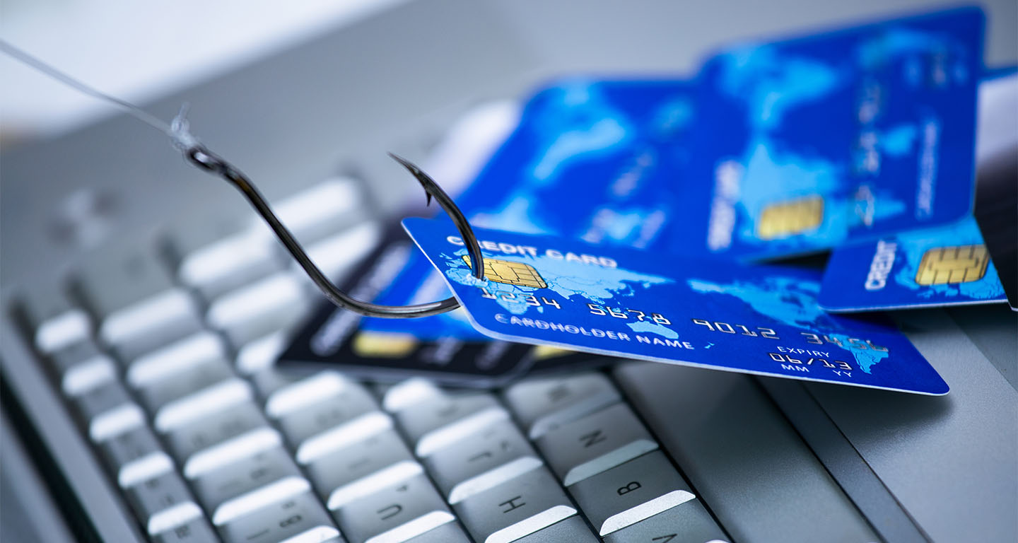 Piles of credit cards with a fish hook on computer keyboard.