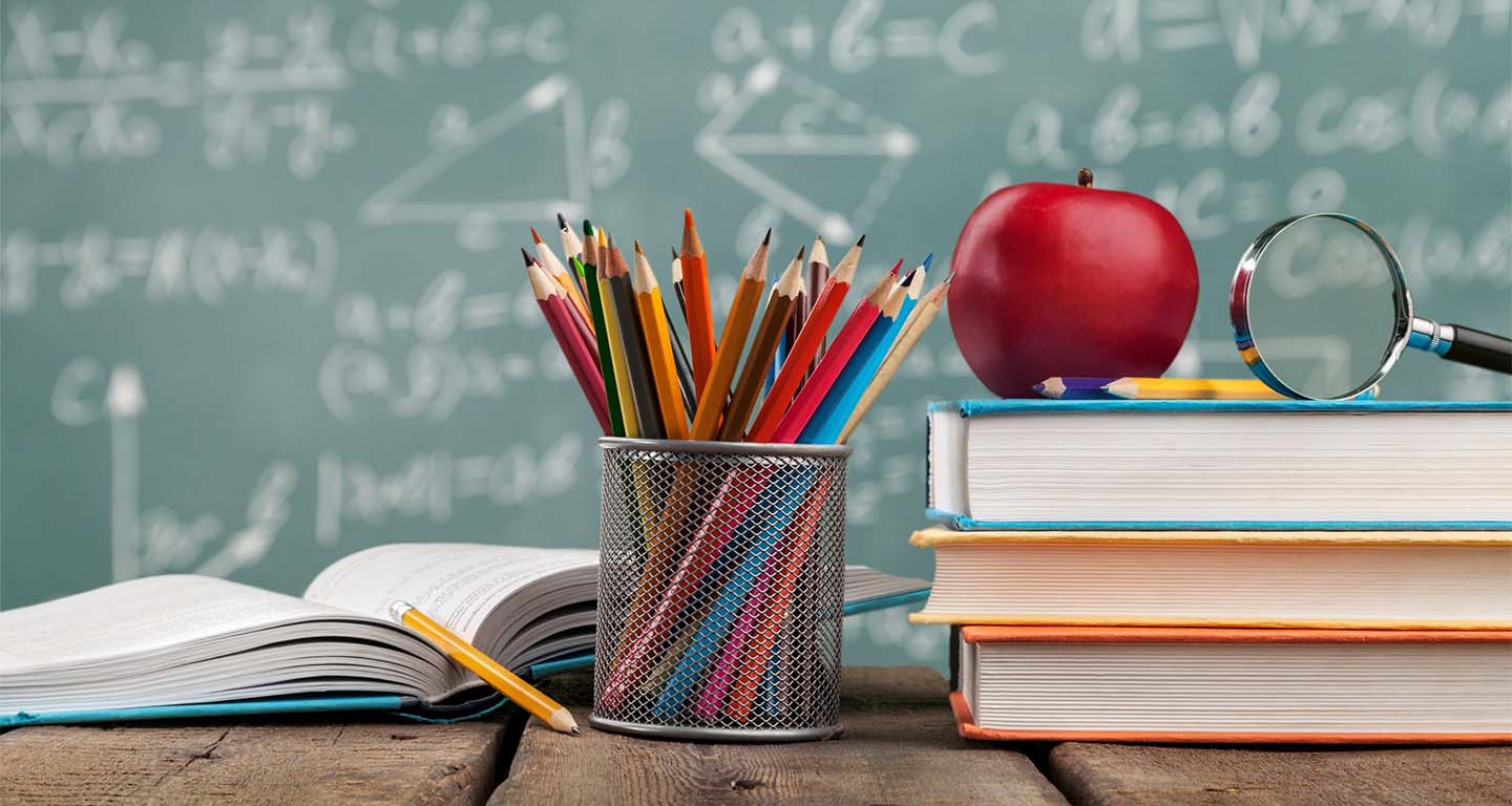 School desk with an apple, books and colored pencils